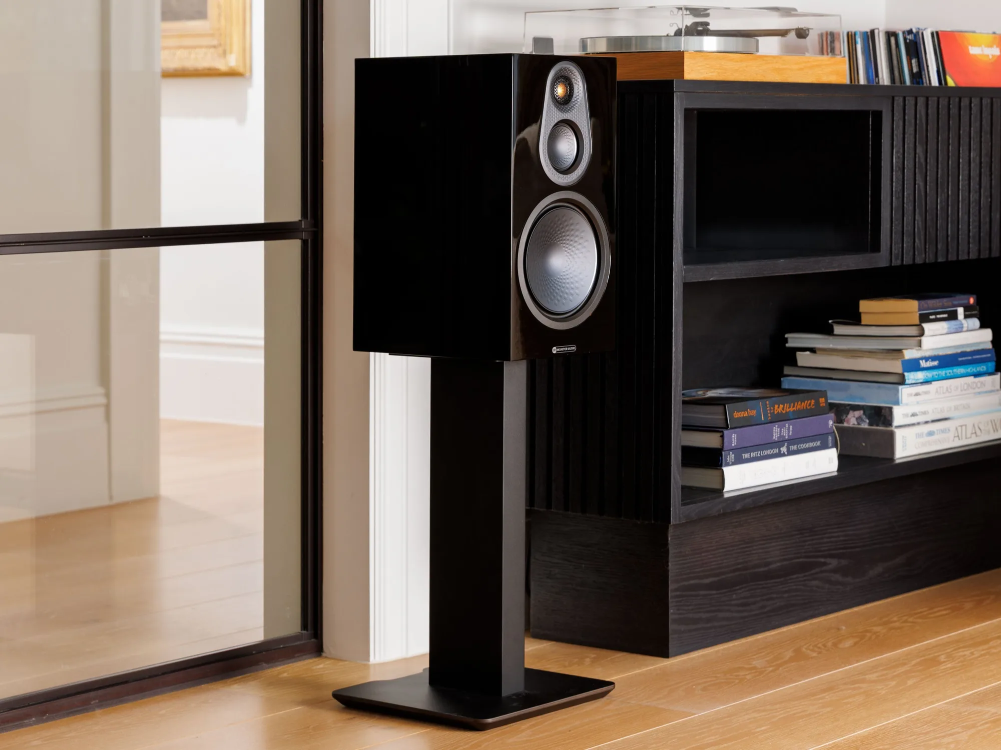 Bafle Monitor Audio Silver 100 8G sobre un pie junto a una biblioteca